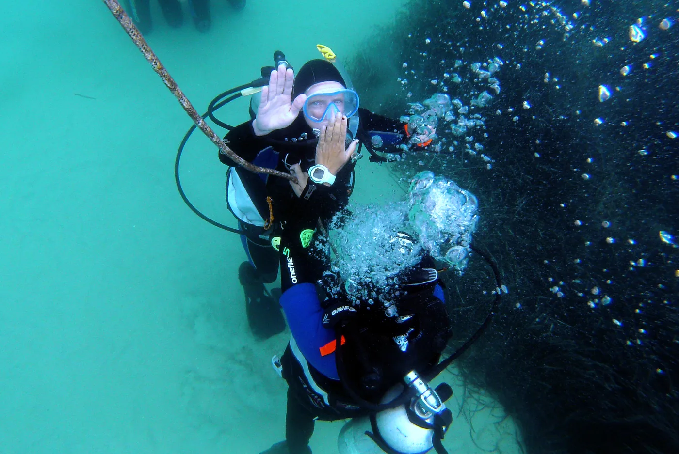 Divers practising underwater hand signals beside a descent line