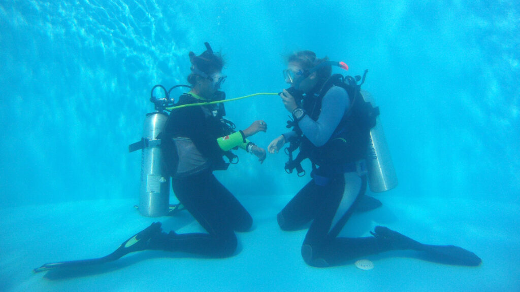 Scuba instructor demonstrating a alternative air source use to scuba divers underwater.